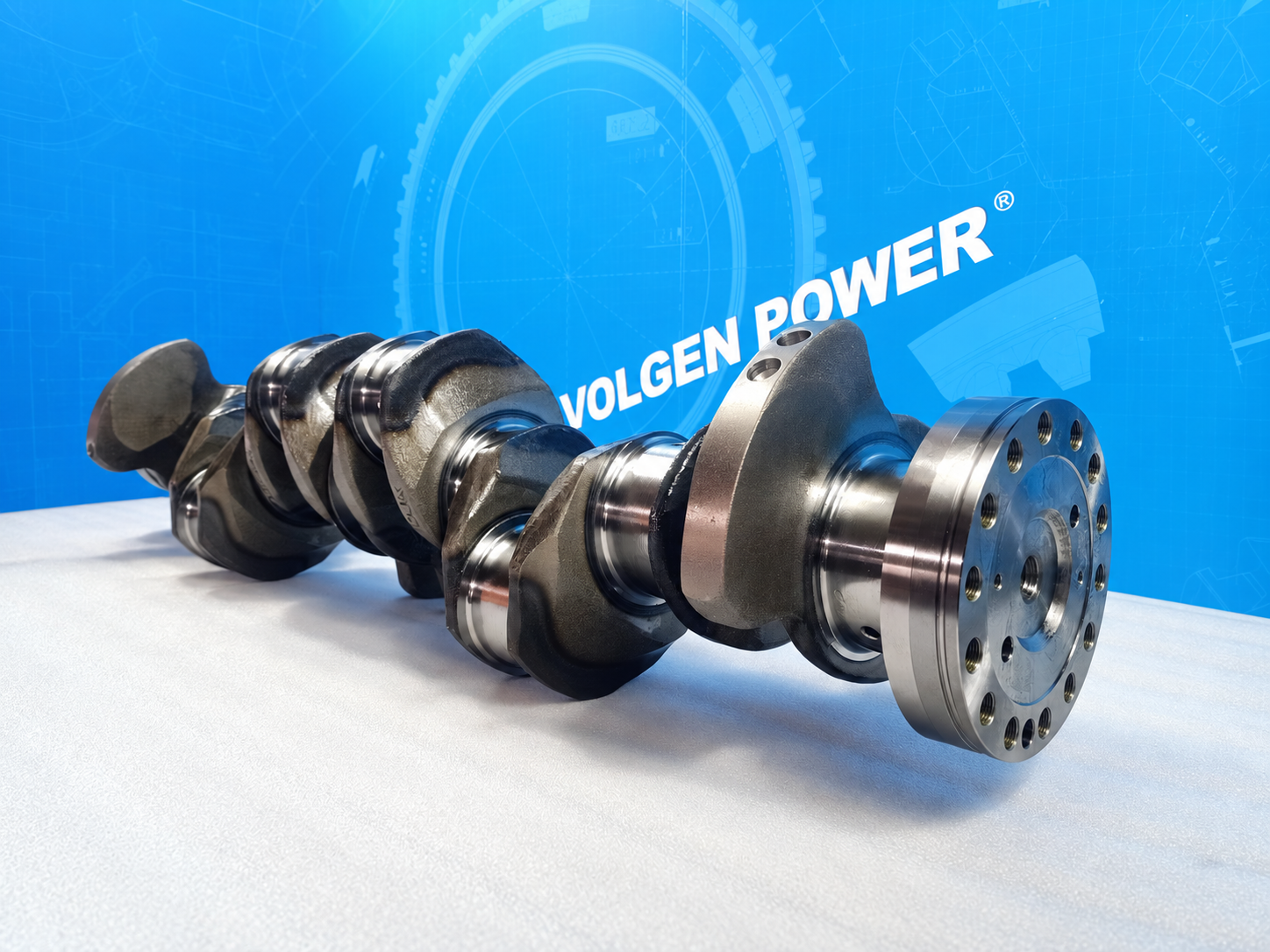 Crankshaft with visible counterweights, journals and end flange against a blue Volgen Power background